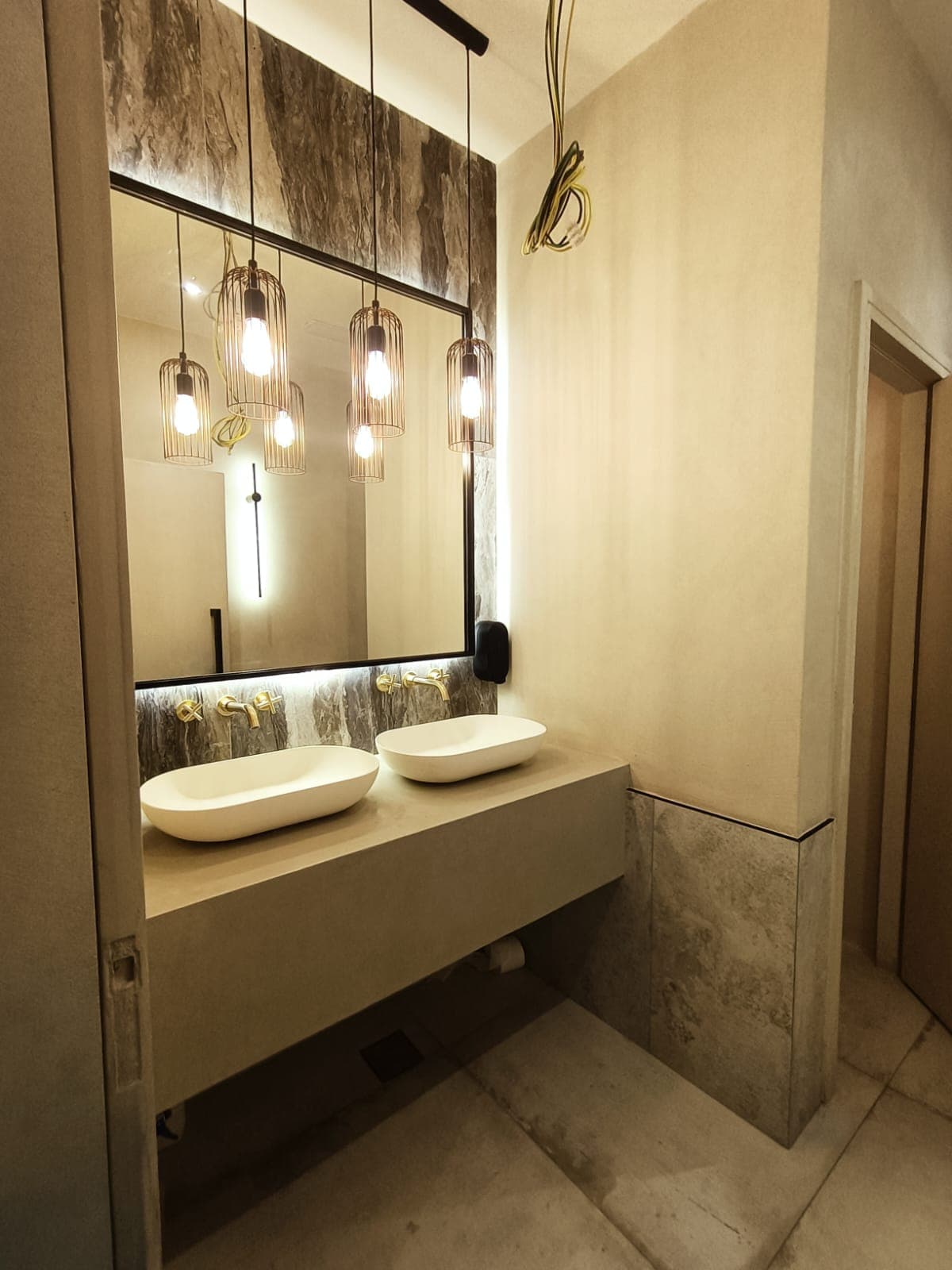 Double-vanity ensuite bathroom with book-matched stone and cage pendant lights